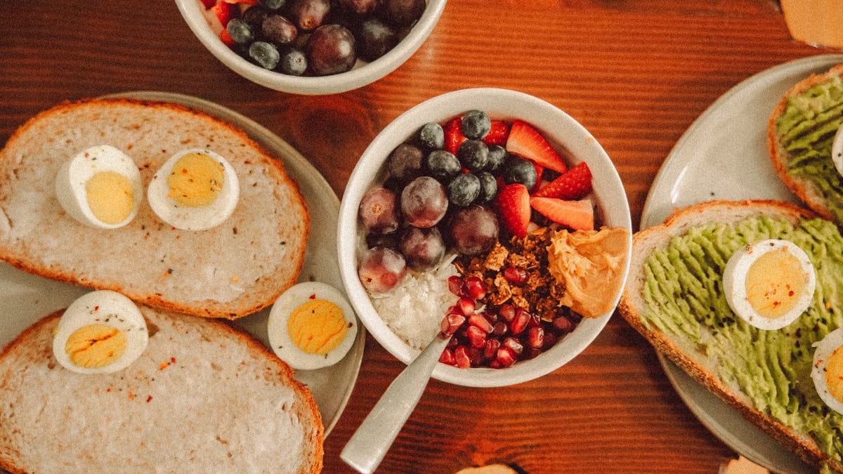 A fresh and vibrant breakfast flat lay featuring a yogurt bowl with fruits and toast with eggs and avocado.